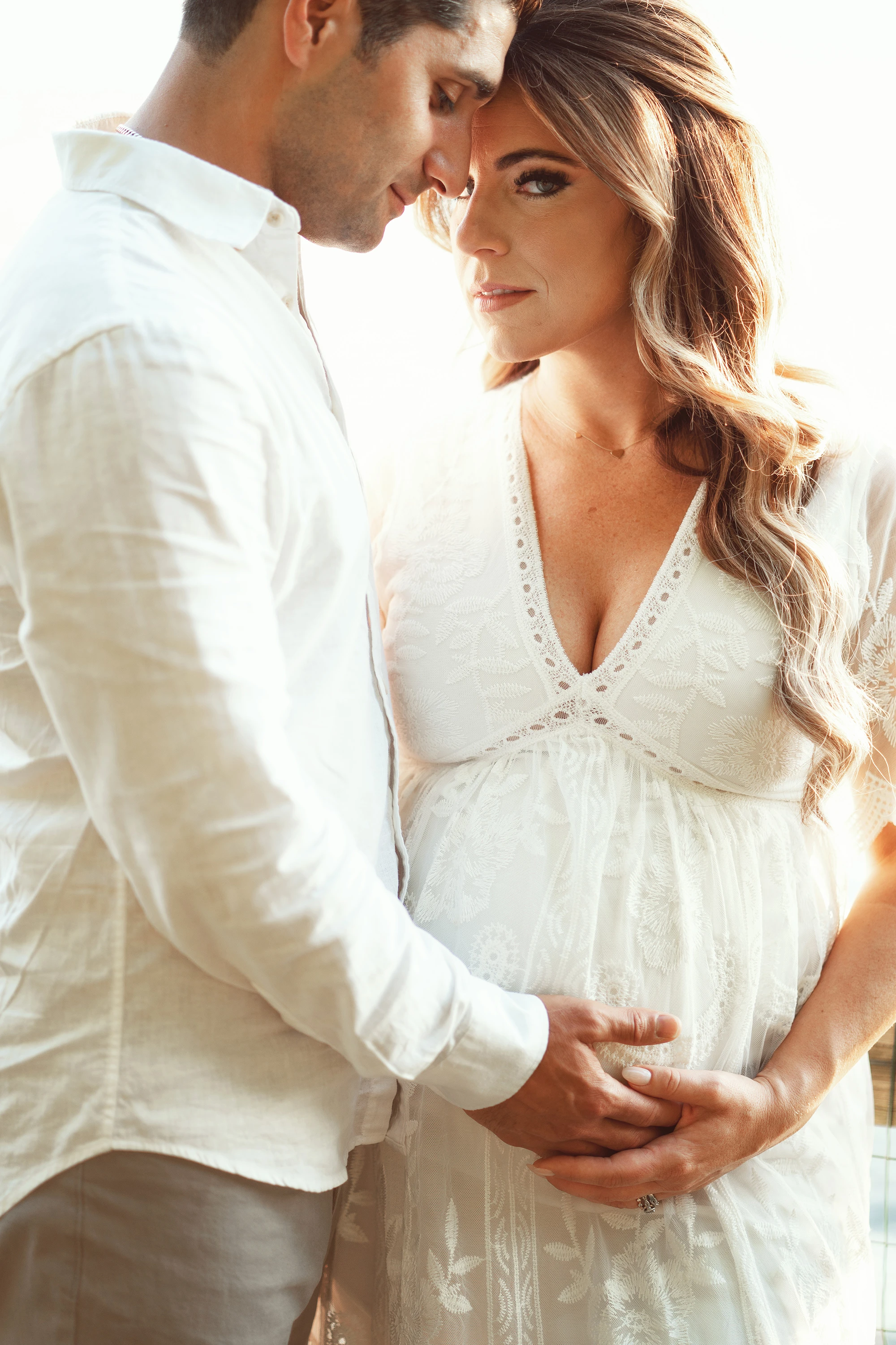 woman in white maternity gown leaning her head against her husband's head