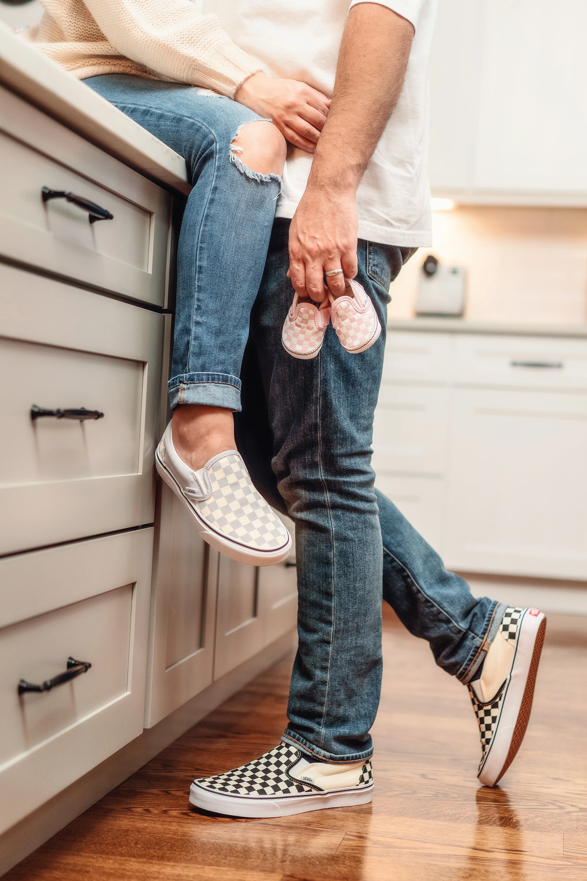 maternity photo of man hugging woman holding baby shoes