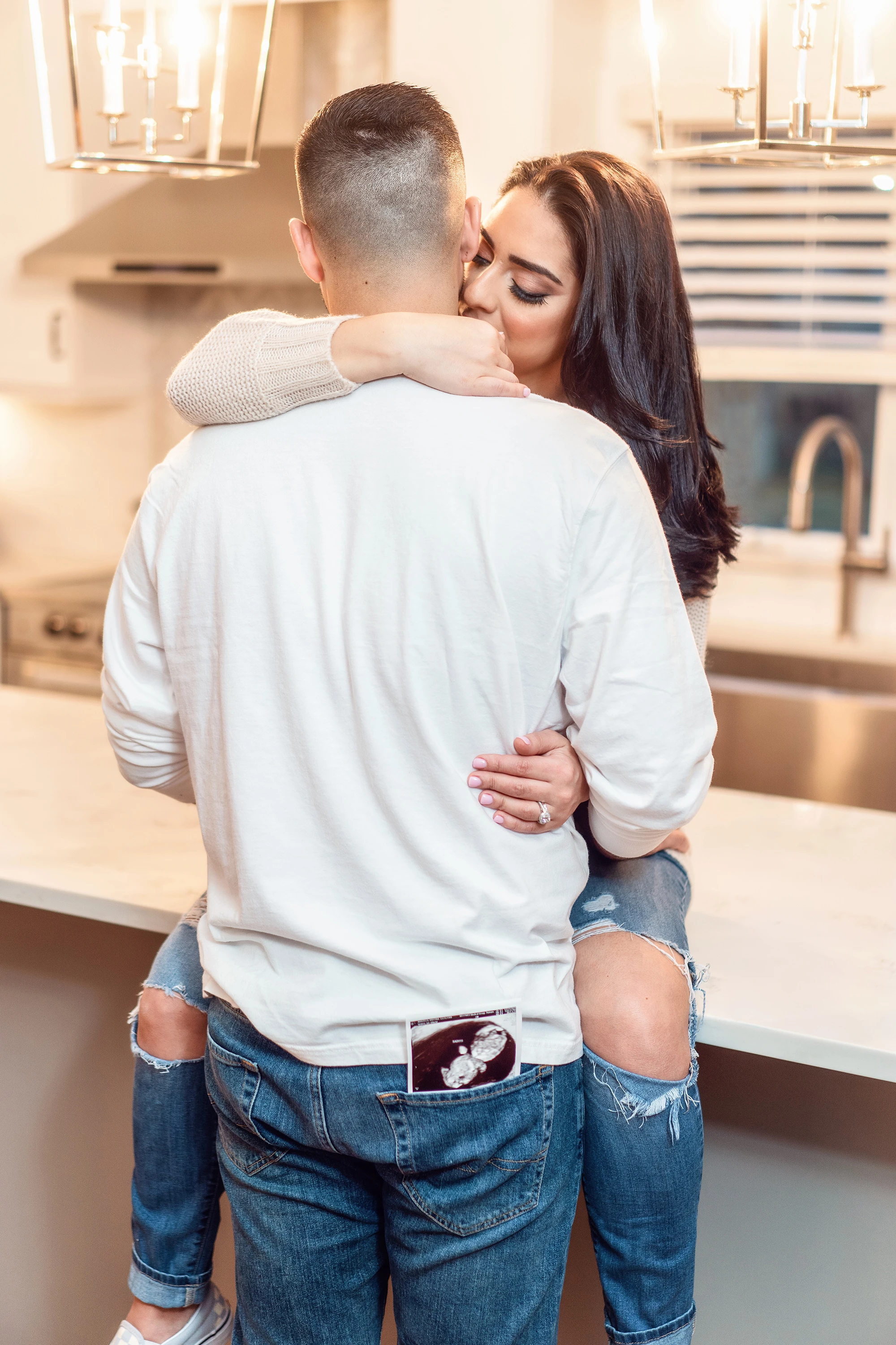 couple kissing with sonogram in the man's back pocket as he hugs his wife