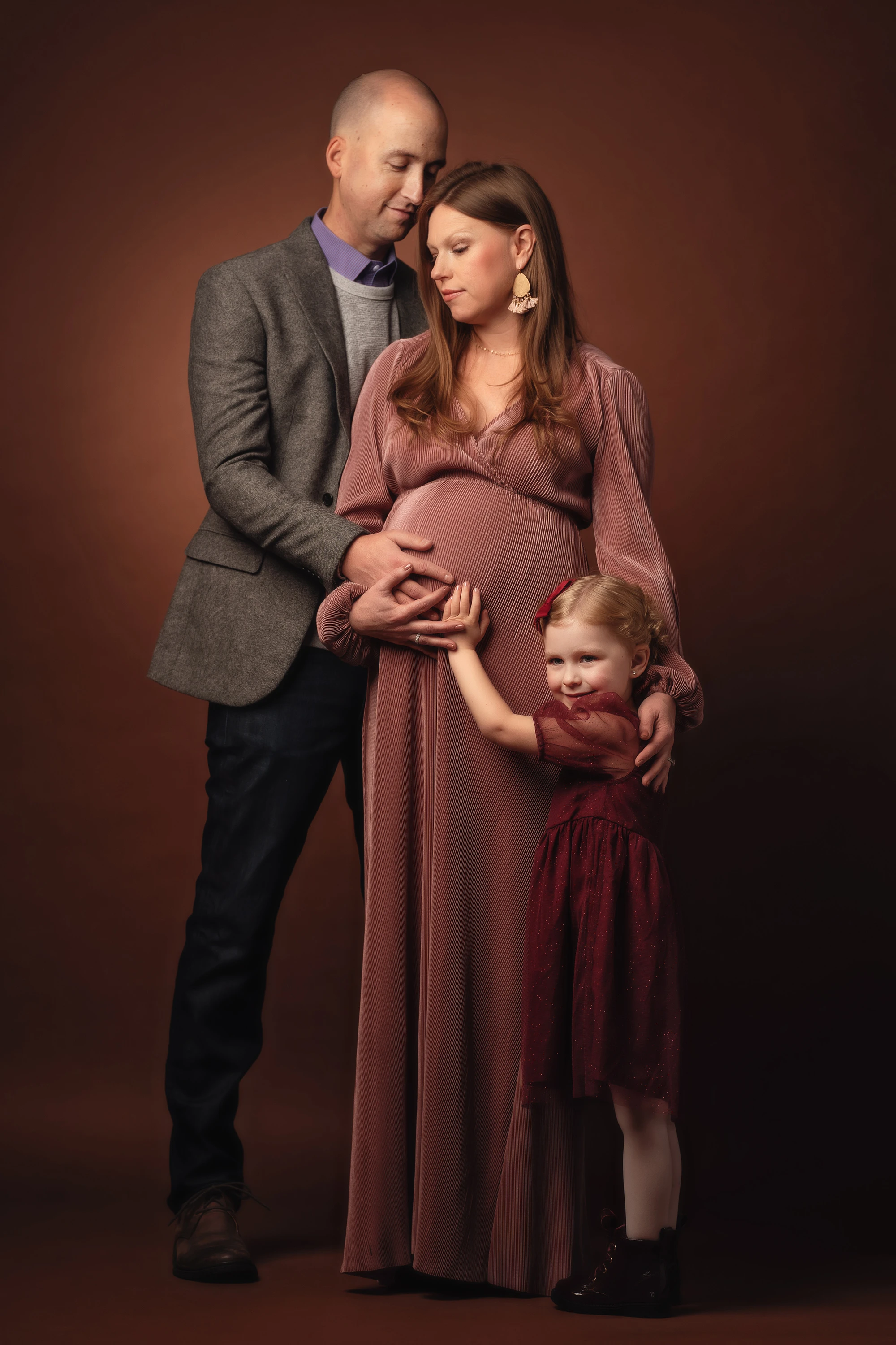 family photo with man, woman and little girl holding pregnant mother's stomach