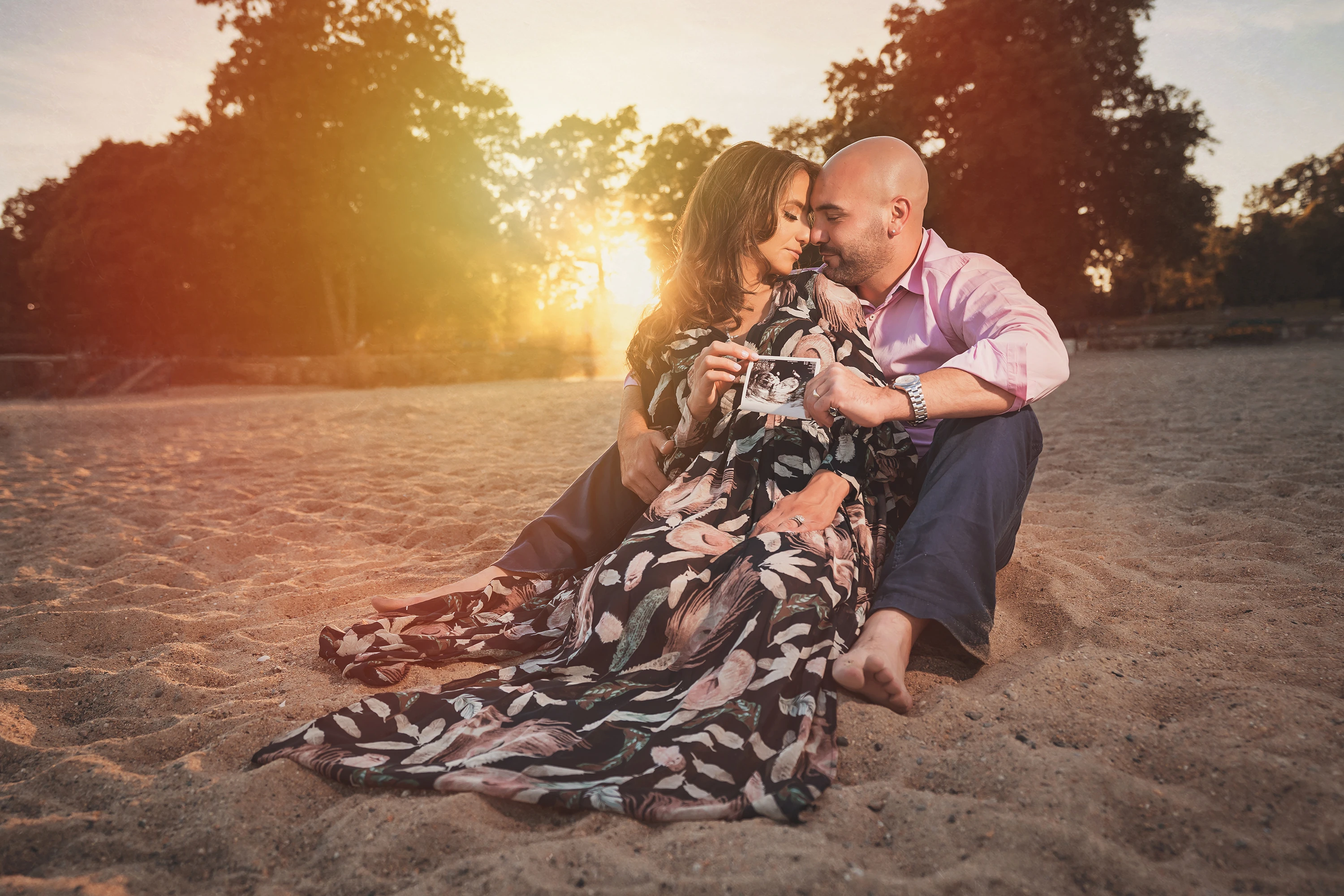 maternity photo of couple sitting on beach at sunset