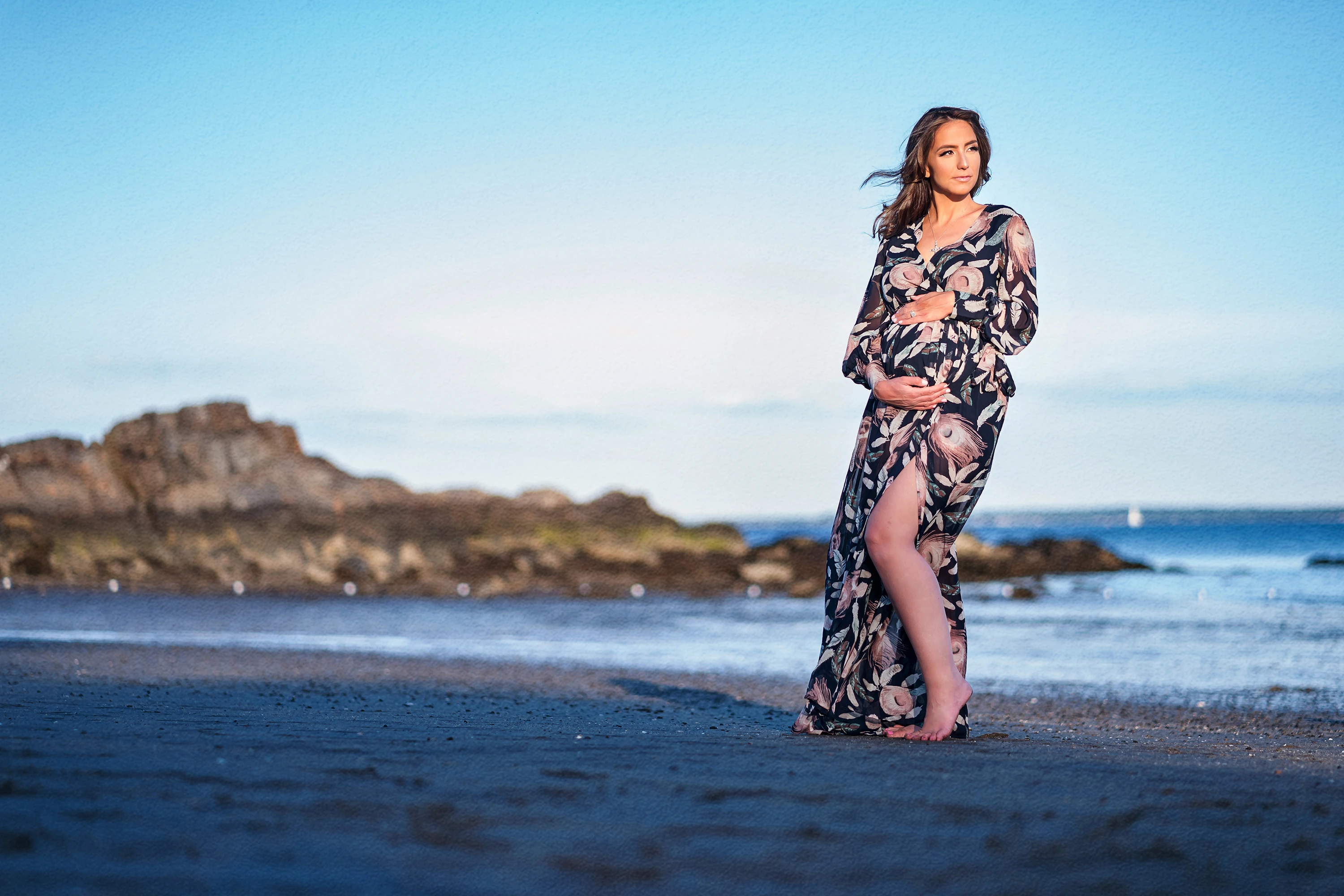 maternity photo of woman in flower dress standing in front of the water