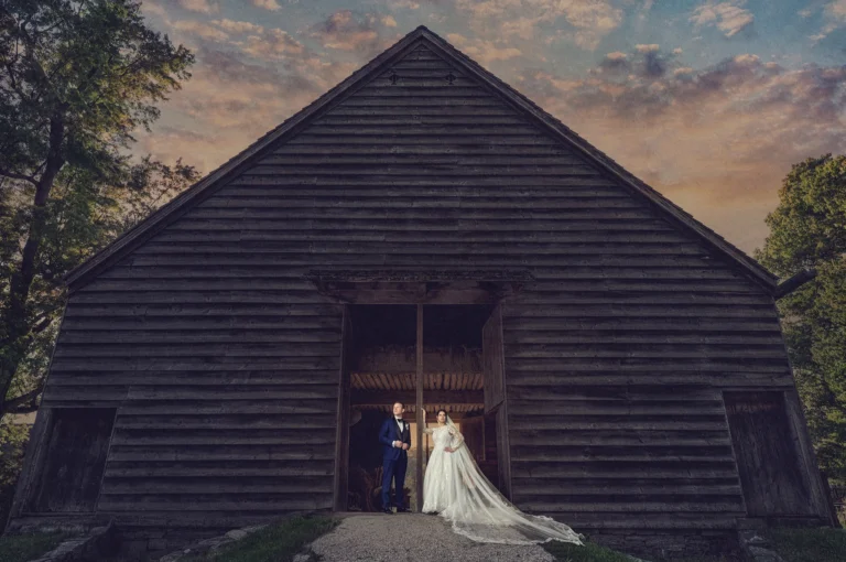 Photo of bride and groom at Sleepy Hollow NY wedding standing in front of barn in dress and tuxedo
