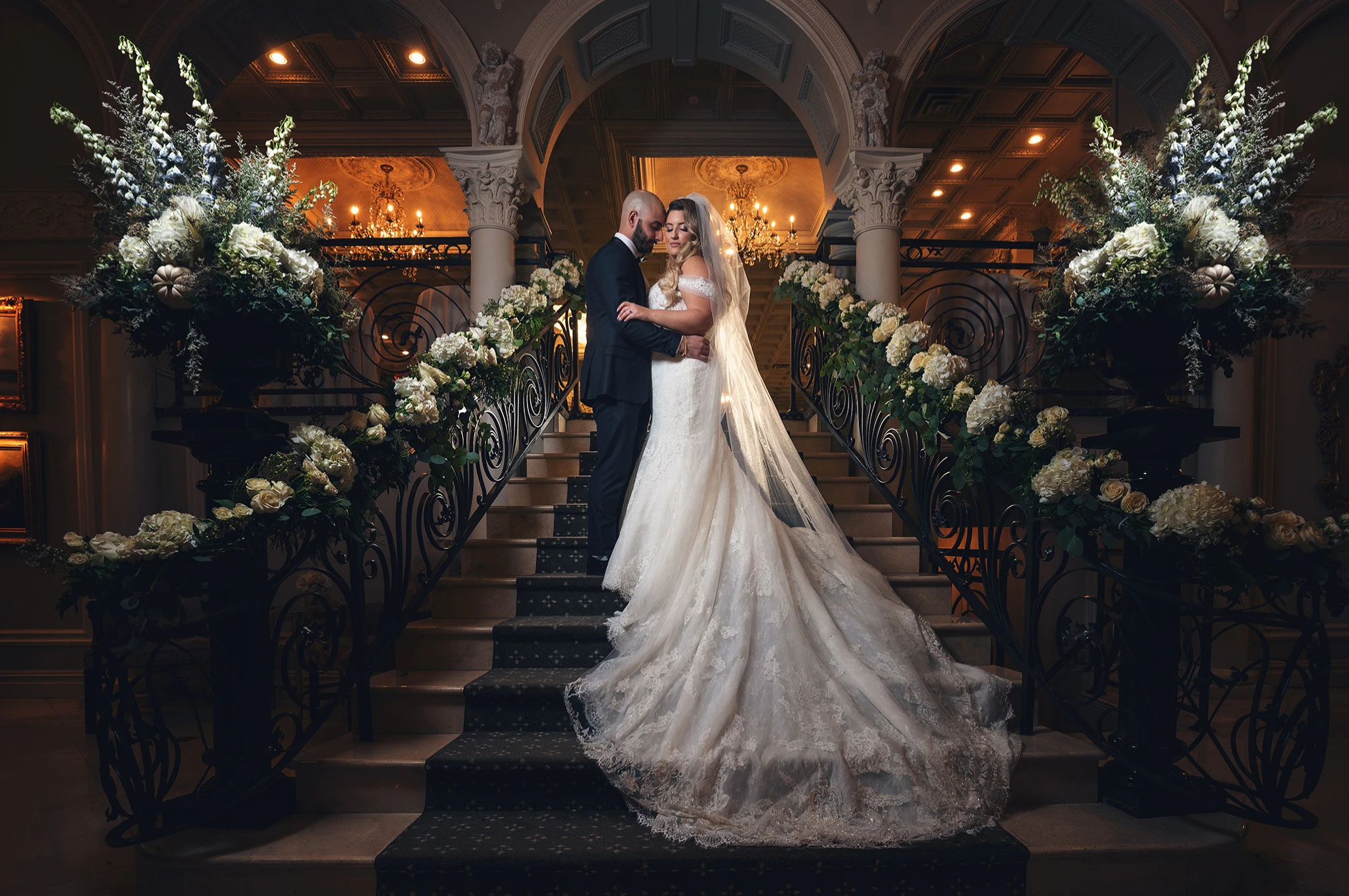 Photo of bride and groom in gown and tuxedo on stairs