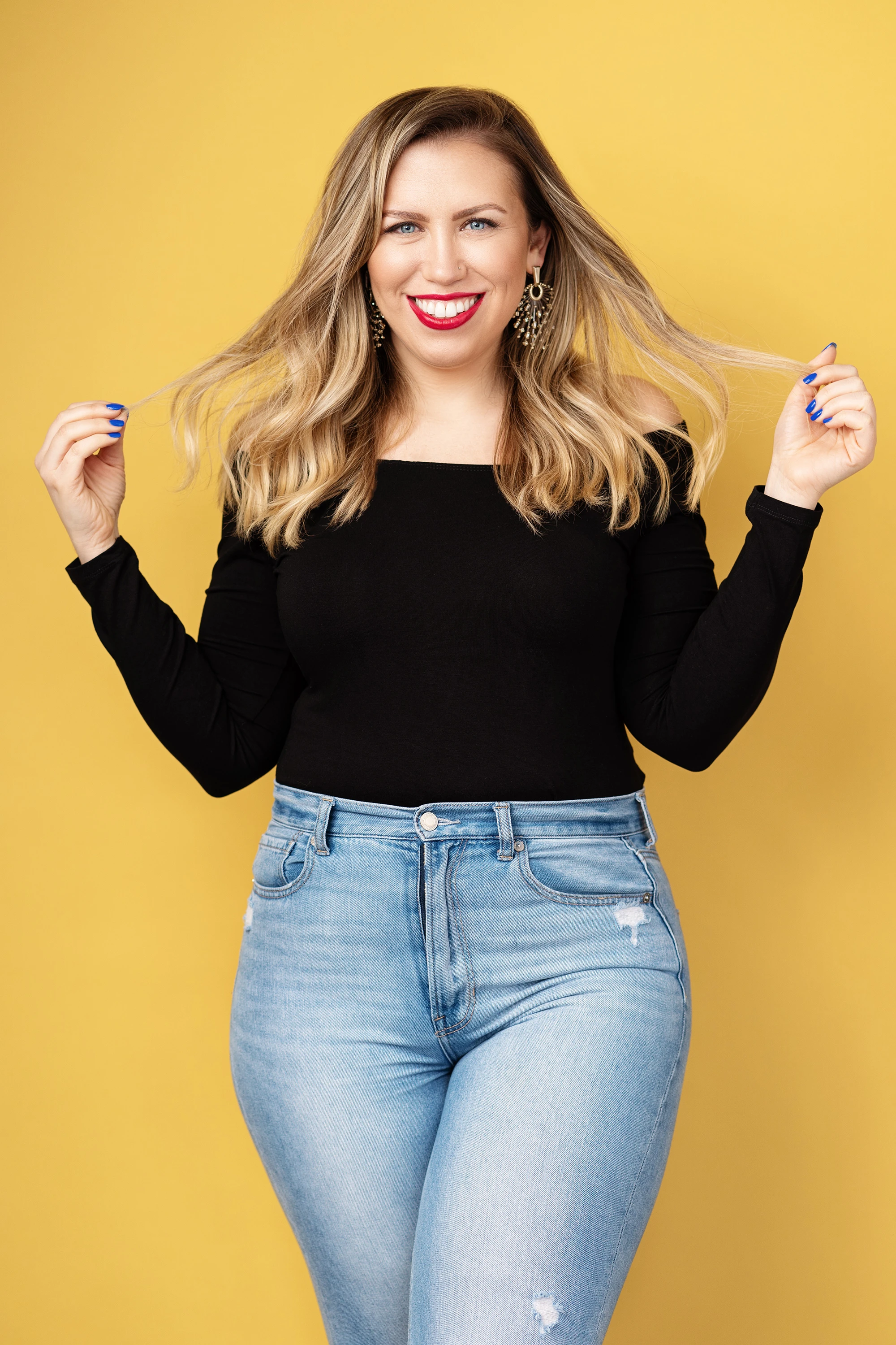 creative portrait of blonde woman with jeans and black shirt in front of colorful yellow backdrop