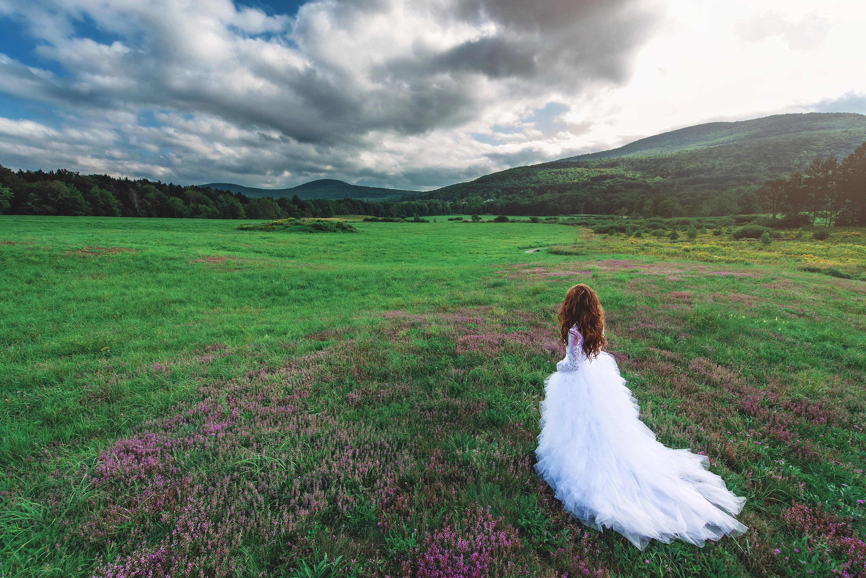 creative portrait of woman in wedding dress looking out towards a beautiful green mountain and hills