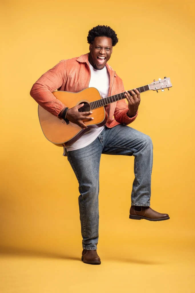 creative portrait of a musician in jeans and button down shirt posing with orange photo backdrop