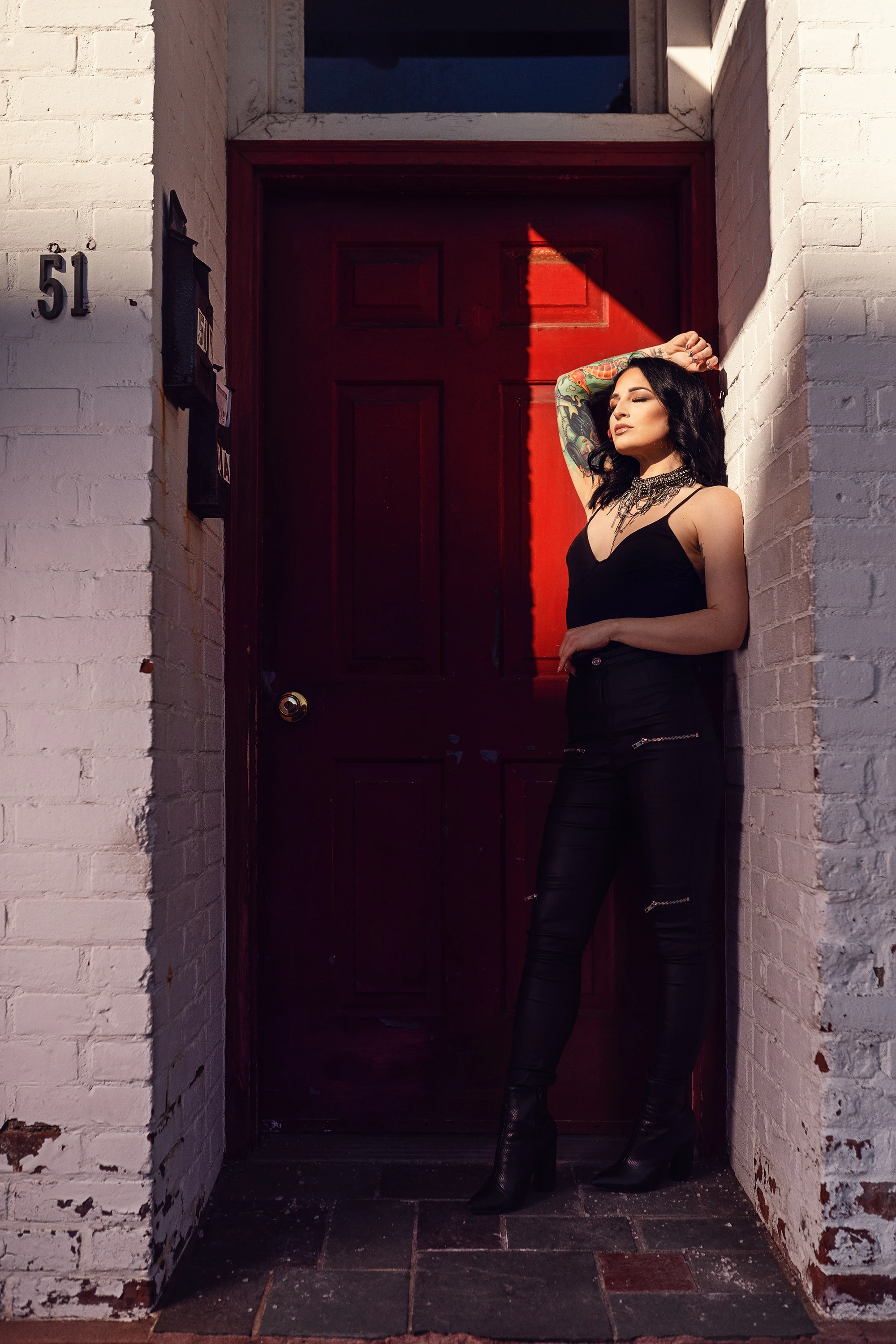 portrait of woman leaning up against white brick wall in a black halter top