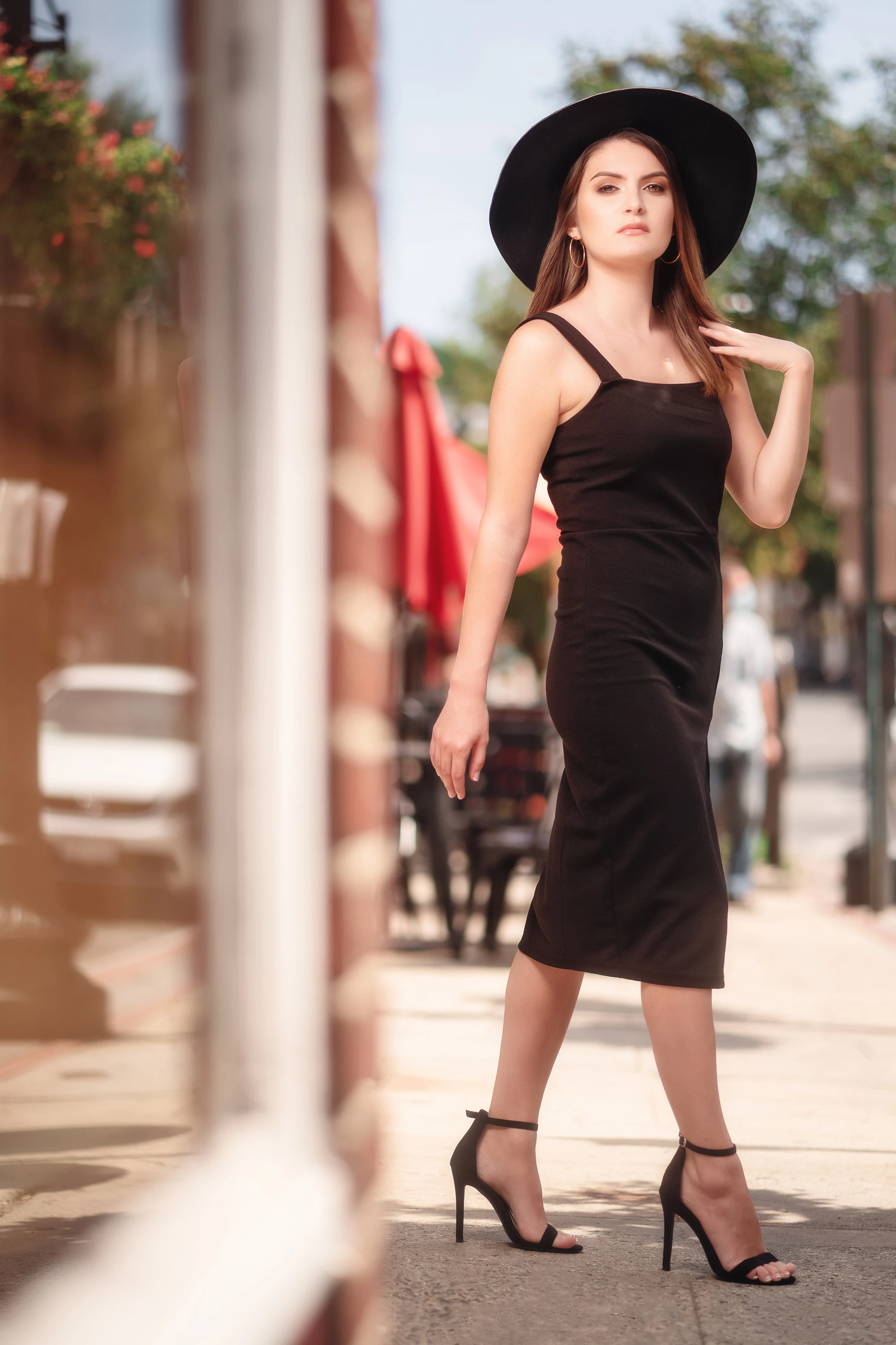 creative portrait of woman in black dress, black hat, and black high heels posing outdoors