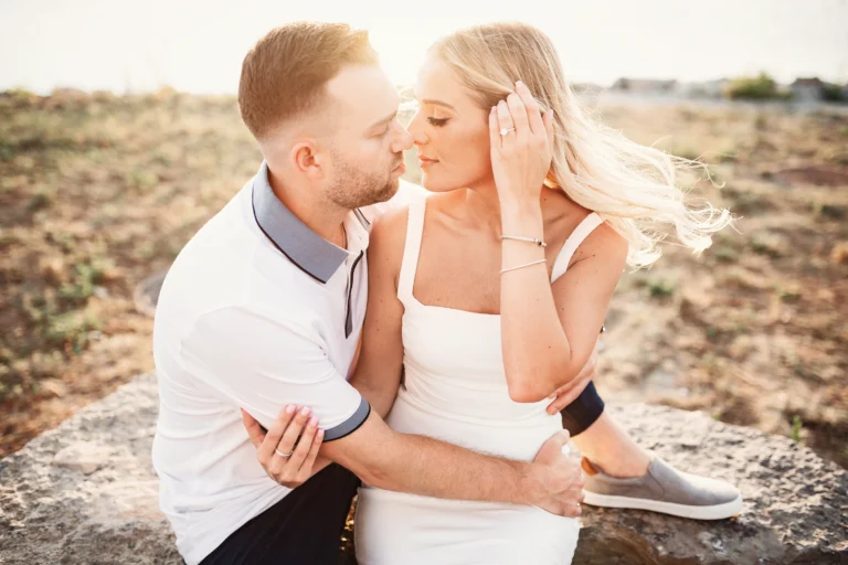 Couple posing for engagement photos on beach in white dress and white polo