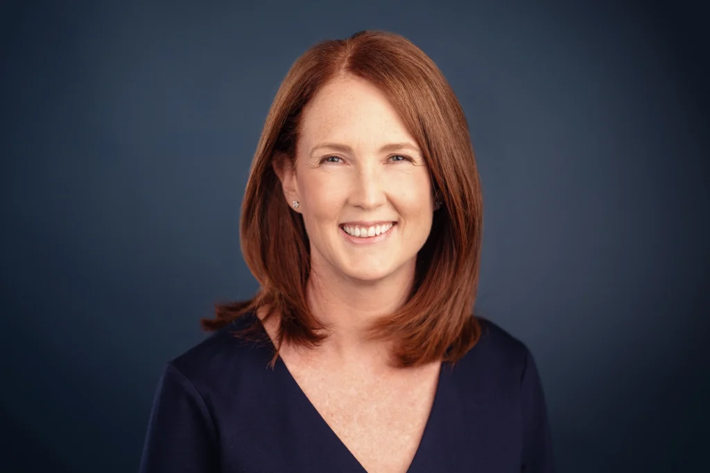 Professional headshot of woman wearing a blue sweater with a blue background
